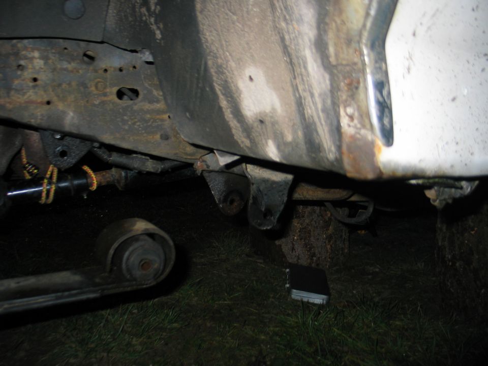 Close-up of rusted vehicle frame and suspension parts, including a leaf spring and shock absorber mount