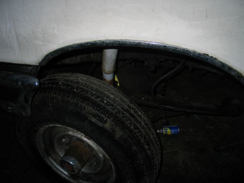 1984 Ford Bronco - A can of lubricant rests on the ground near the rear tire and suspension of a vehicle.