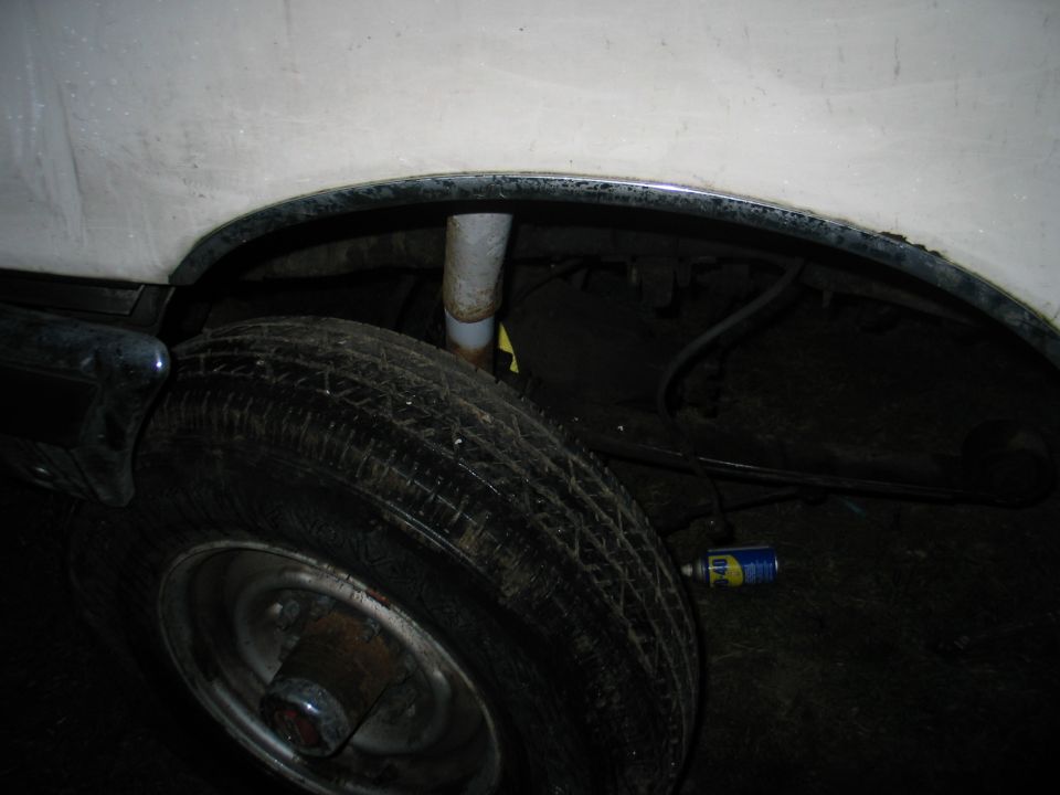 Close-up of rear wheel well with shock absorber and tire visible. Can of lubricant on the ground