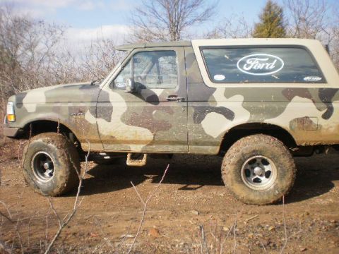 1995 Ford Bronco - Side view of a 1995 Ford Bronco in camouflage paint, parked off-road.
