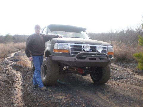 1995 Ford Bronco - A man stands next to a modified Ford Bronco on a dirt road.