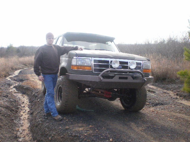 Muddy lifted Ford SUV with black steel bumper and driving lights on dirt trail
