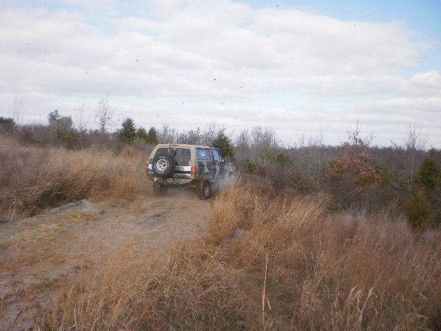 Camo-painted SUV with rear spare tire driving down a muddy off-road trail