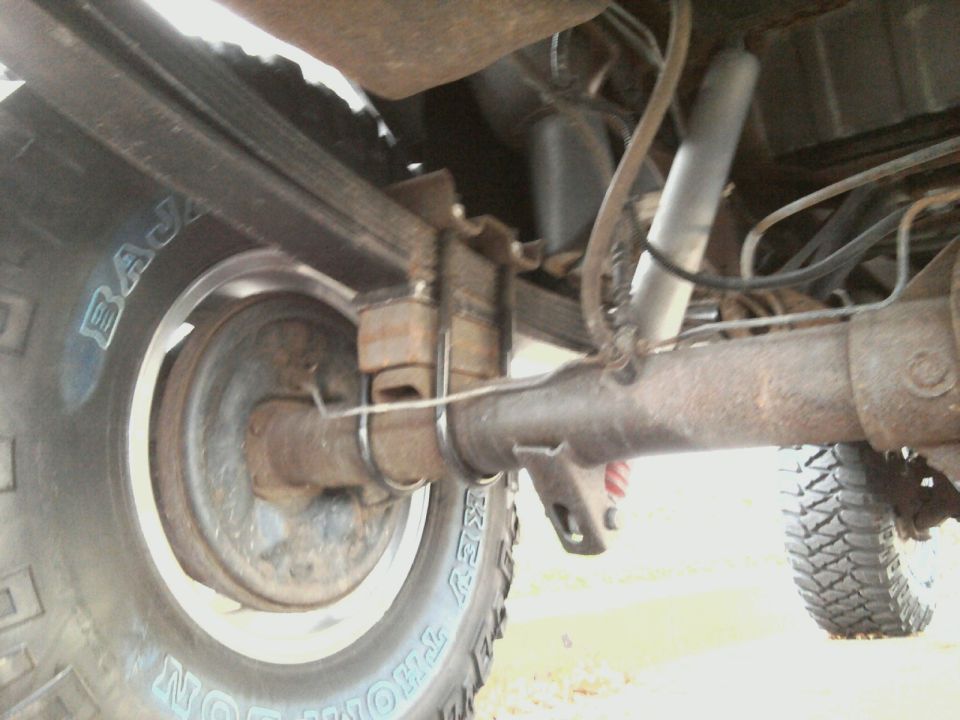 Close-up of a vehicle's rear axle, leaf springs, and shock absorber. Tire sidewall reads 'BAJA'