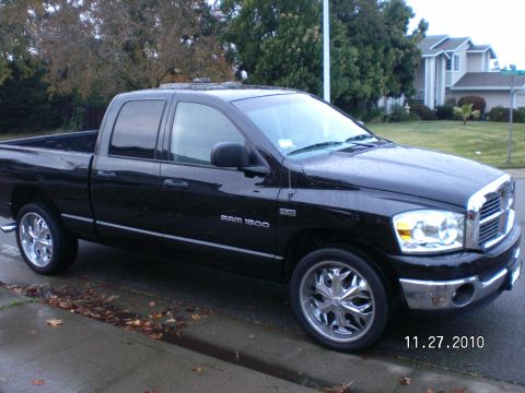 1996 Ford Bronco - A black Dodge Ram 1500 pickup truck is seen from a 3/4 front angle, parked on a wet street with custom chrome wheels.