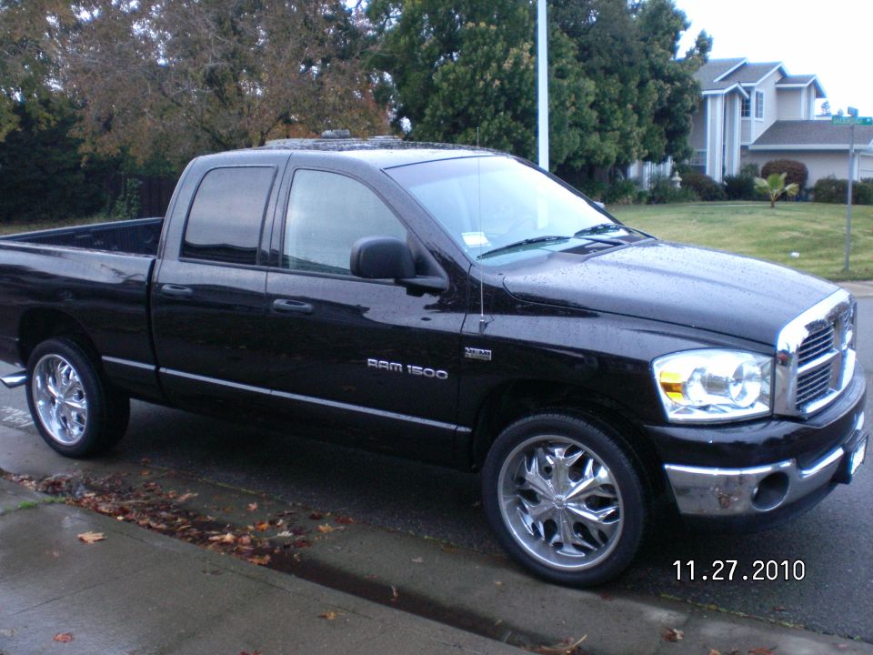 Black Dodge Ram 1500 pickup truck with chrome wheels parked on a wet street