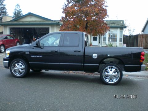 1996 Ford Bronco - A black Dodge Ram 1500 pickup truck is parked on a residential street with a house and trees in the background.