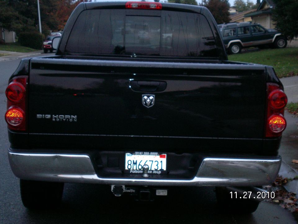 Black Dodge Ram pickup truck rear with 'Big Horn Edition' badge and license plate 8M66731. Another SUV is parked on a hill in the background
