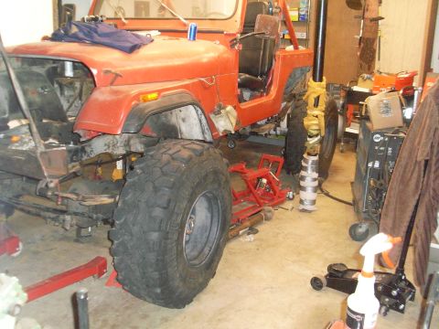 1985 Jeep CJ7 - This orange Jeep CJ is in a garage with its front fender removed and is supported by jack stands.