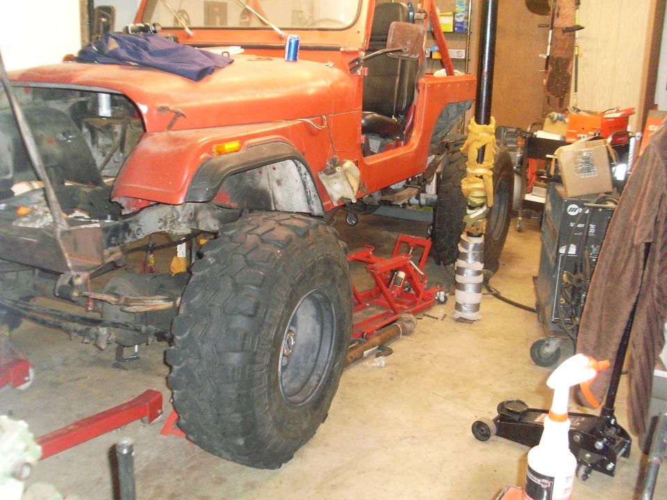 Orange Jeep CJ in garage, front fender removed, large tires, on jack stands