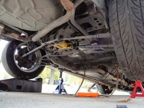 1995 Ford Taurus - The undercarriage of a vehicle is visible, supported by jack stands and ramps, with an oil pan beneath.