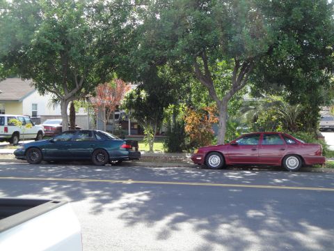 1995 Ford Taurus - A maroon 1995 Ford Taurus is parked on the side of the road next to a dark green sedan.