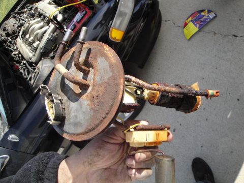 1995 Ford Taurus - A person holds a corroded fuel pump assembly, with the engine bay of a dark-colored car visible behind it.