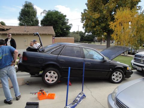 1995 Ford Taurus - A dark blue 1995 Ford Taurus sedan is parked with its trunk and hood open, possibly undergoing maintenance.