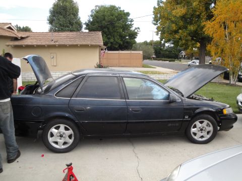 1995 Ford Taurus - A dark blue 1995 Ford Taurus sedan is parked with its hood and trunk open, showing its interior and engine bay.