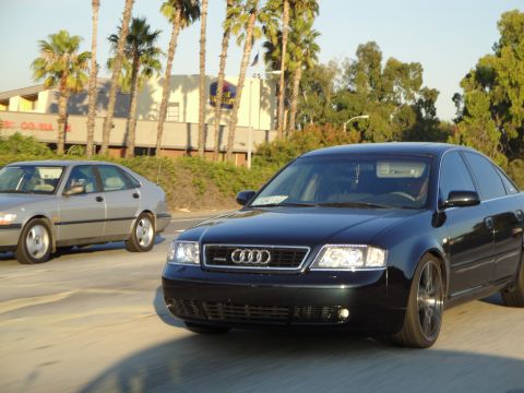 1995 Ford Taurus - Two sedans, a black Audi and a silver Saab, travel down a highway under a clear sky.
