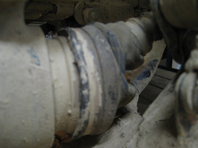 Mud-caked CV axle shaft and pleated rubber boot seen from underneath a vehicle