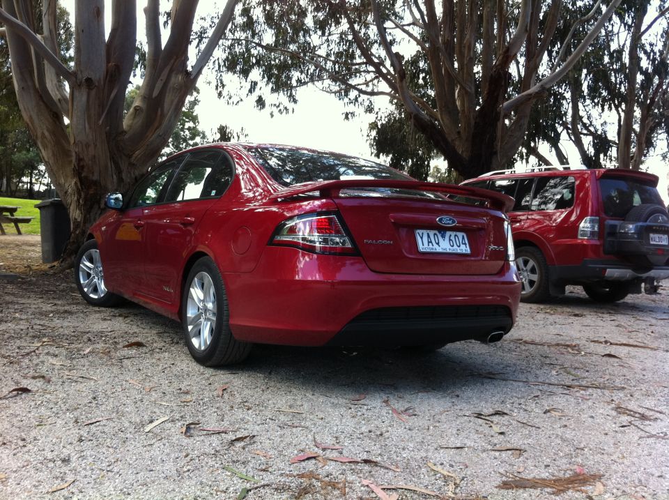 Rear view of red Ford Falcon sedan parked next to a red SUV. License plate YAQ 604