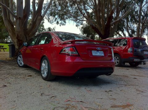 2010 Ford Falcon - A red 2010 Ford Falcon sedan is parked next to a red SUV under trees.