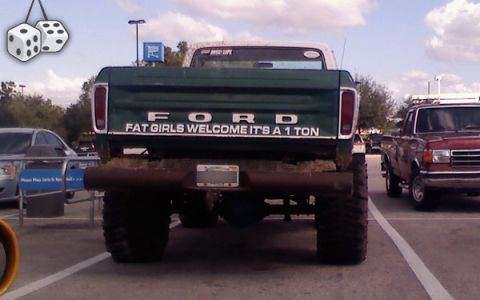 1988 Ford Bronco - Rear view of a lifted green Ford pickup truck with a humorous message on the tailgate.