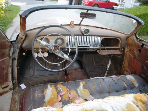1986 Ford Bronco - The interior of a dilapidated 1951 Chevrolet convertible, showing significant rust and wear on the seats and dashboard.