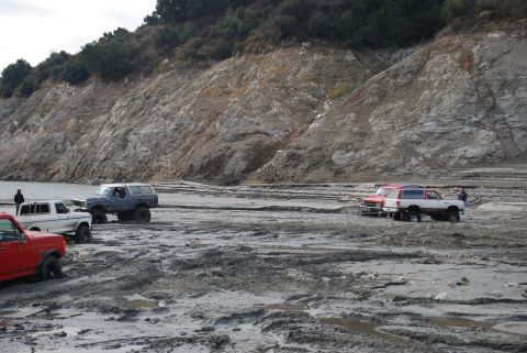 1996 Ford Bronco - Multiple vehicles navigate a challenging muddy landscape with a steep, rocky incline in the background.
