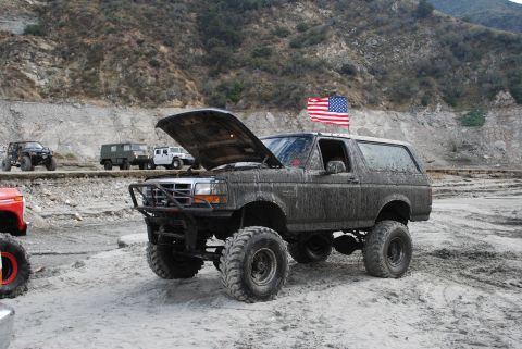 1996 Ford Bronco - Muddy 1996 Ford Bronco with hood up and flag flying, parked in a dirt lot with other vehicles.