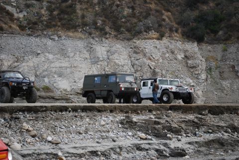1996 Ford Bronco - Several vehicles are stopped on a narrow dirt road beside a steep, rocky embankment.