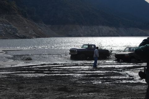 1996 Ford Bronco - Two trucks are stuck in the mud near a lake, with one person observing the scene.