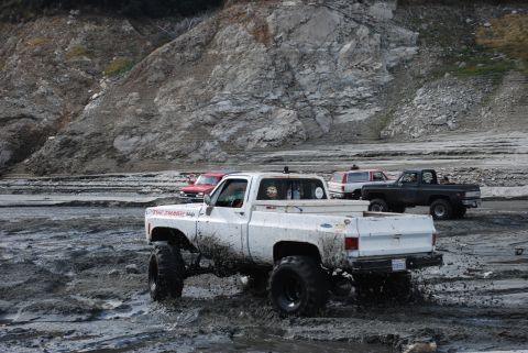 1996 Ford Bronco - Multiple trucks navigating a muddy terrain with a rocky hillside in the background.