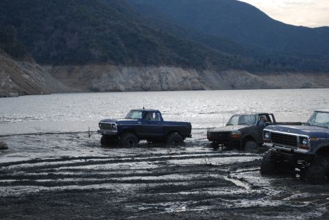 1996 Ford Bronco - Several Ford pickup trucks, including a blue 1979 F-150, are stuck in the mud near a body of water.