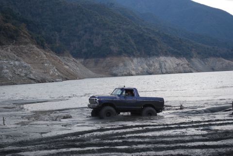 1996 Ford Bronco - A lifted 1978 Ford F-150 navigates a muddy shoreline next to a body of water, with a mountainous backdrop.