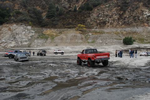 1996 Ford Bronco - Several off-road vehicles are gathered in a muddy, rocky terrain with a hillside in the background.