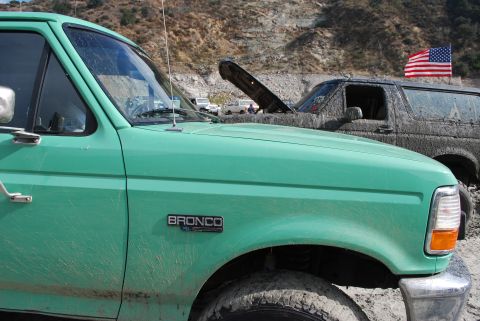 1996 Ford Bronco - A green 1996 Ford Bronco is seen in profile, with another muddy Bronco in the background under an American flag.