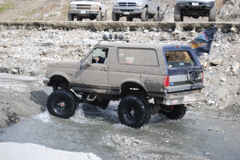 1996 Ford Bronco - A lifted Ford Bronco navigates a rocky stream with other trucks in the background.