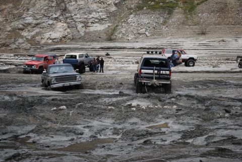 1996 Ford Bronco - Multiple off-road vehicles navigate a challenging muddy terrain with rocky hills.