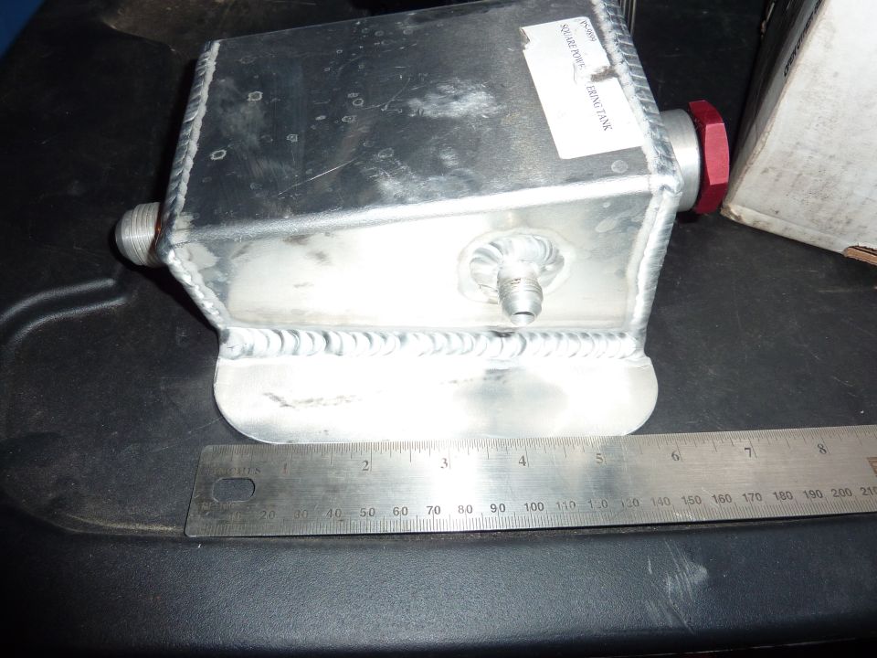 Aluminum coolant overflow tank with a red cap and a label that says "SQUARE PORCE" and "RESERVOIR TANK". A ruler is in front of it