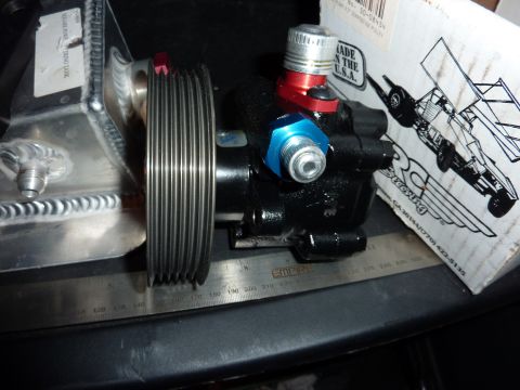 1971 Ford Mustang - Close-up of a black power steering pump with a pulley and an aluminum tank, resting on a ruler.