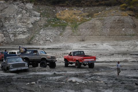 1996 Ford Bronco - Several off-road vehicles are parked in a muddy, rocky area with a large hill in the background.