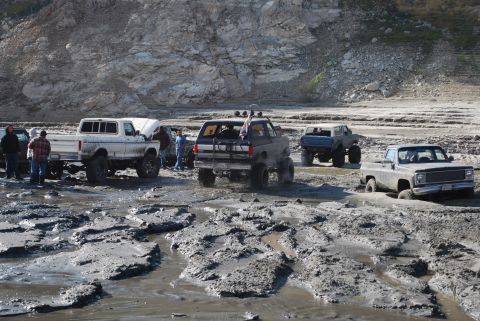 1996 Ford Bronco - Multiple off-road vehicles navigate a challenging muddy terrain with a rocky backdrop.
