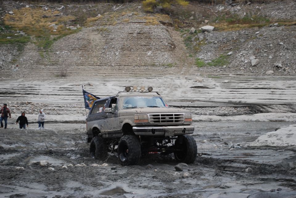 Lifted 1996 Ford Bronco driving through mud with a flag on the back