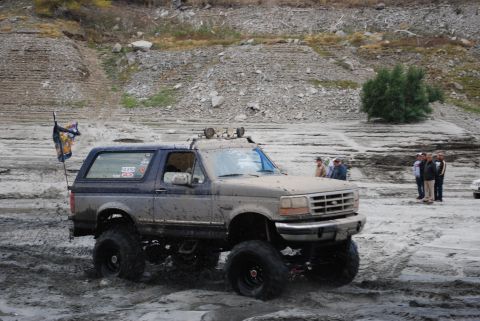 1996 Ford Bronco - A lifted 1996 Ford Bronco navigates a muddy, off-road terrain with a flag attached to its rear.