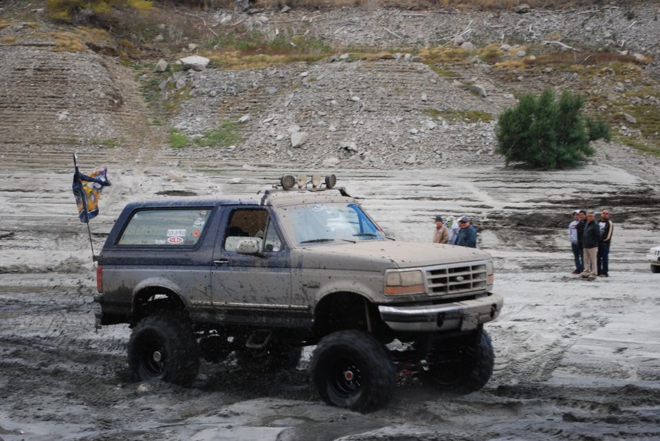 Lifted 1996 Ford Bronco driving through mud with a flag on the back