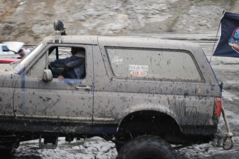 1996 Ford Bronco - Muddy 1996 Ford Bronco navigates off-road terrain, displaying stickers on the rear window.