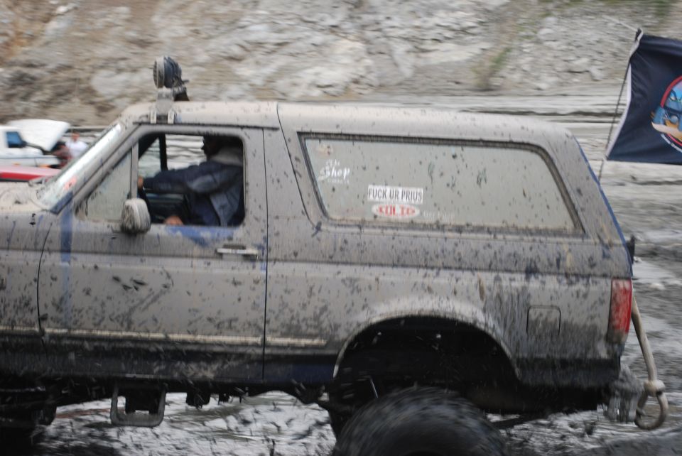1996 Ford Bronco covered in mud, driving off-road with a flag on the back