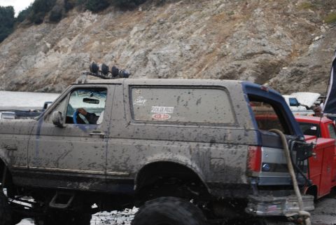 1996 Ford Bronco - This heavily muddied SUV is equipped with off-road lights and appears to be navigating a challenging terrain.