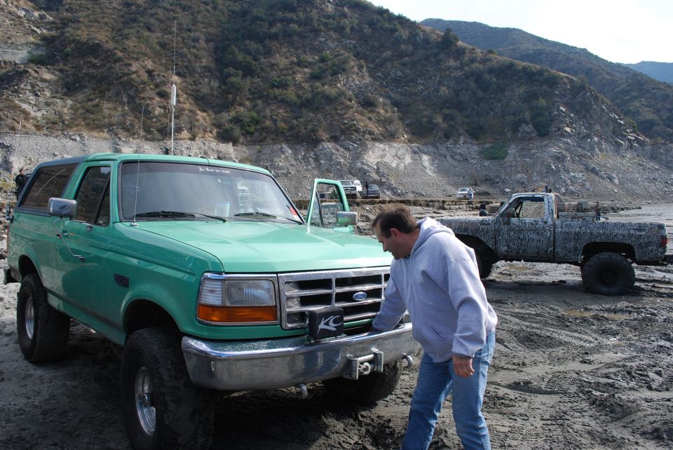 Green Ford Bronco with a winch on the front bumper, parked on a dirt lot with a man inspecting it