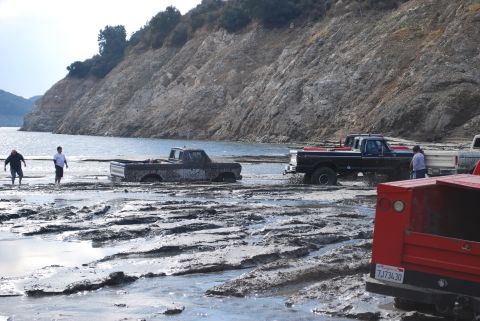 1996 Ford Bronco - Multiple trucks are stuck in the mud near a lake, with people standing around them.