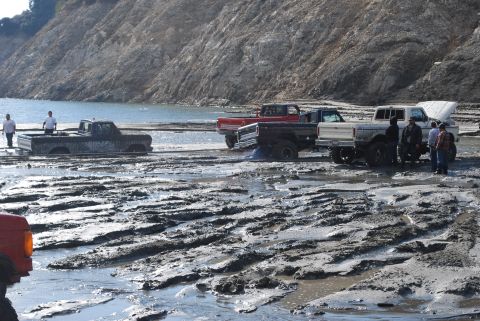 1996 Ford Bronco - Multiple trucks are stuck in the mud, with people standing around them.