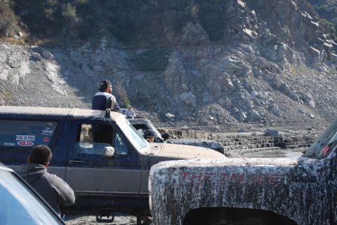 1996 Ford Bronco - Several off-road vehicles are gathered in a rocky, muddy terrain with a steep hillside in the background.